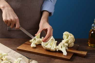 Woman cutting fresh cauliflower at wooden table, closeup