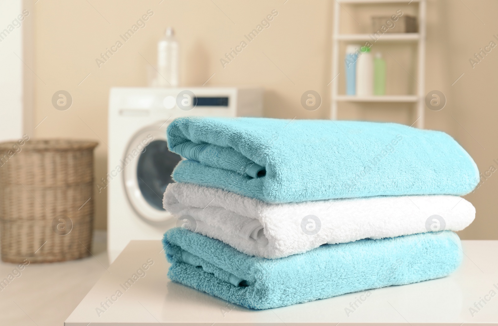 Photo of Stack of clean soft towels on table in laundry room. Space for text