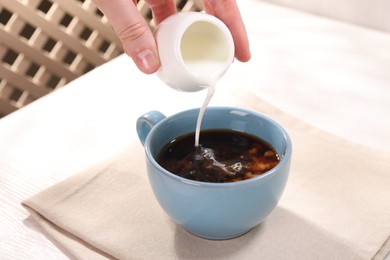 Woman pouring milk into cup with aromatic coffee at white table, closeup