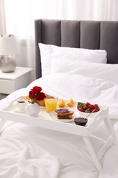 Photo of Tray with delicious breakfast on bed in room