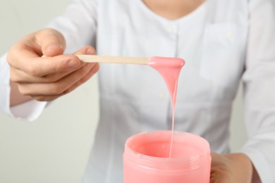 Photo of Woman holding spatula with hot depilatory wax, closeup