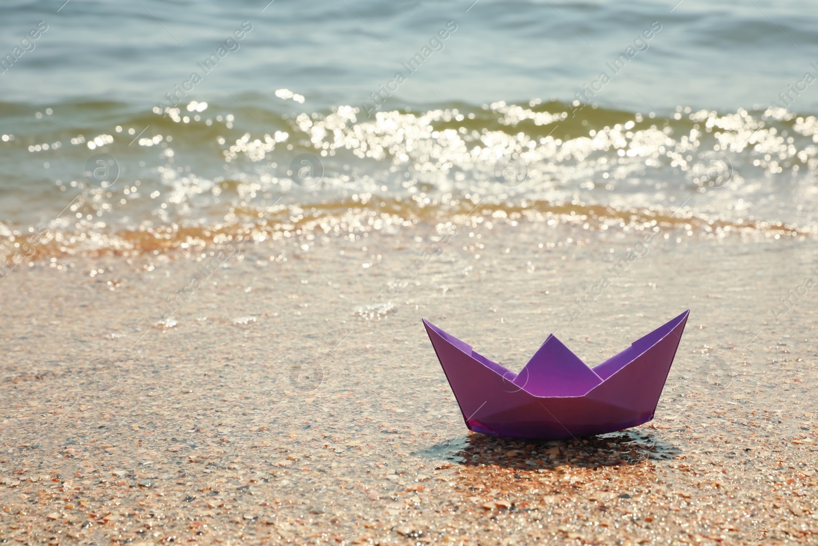 Photo of Purple paper boat near sea on sunny day, space for text