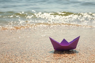Photo of Purple paper boat near sea on sunny day, space for text