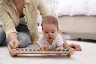 Photo of Cute baby and mother playing with xylophone on floor at home