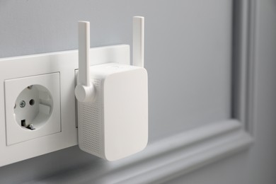 Wireless Wi-Fi repeater on light grey wall, space for text