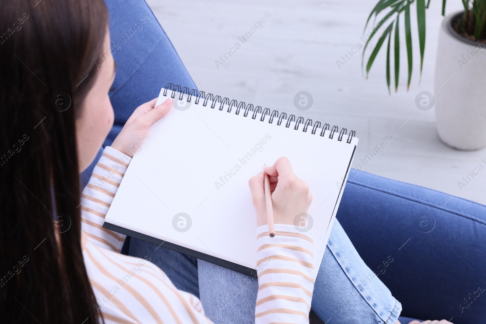 Photo of Young woman drawing in sketchbook indoors, closeup