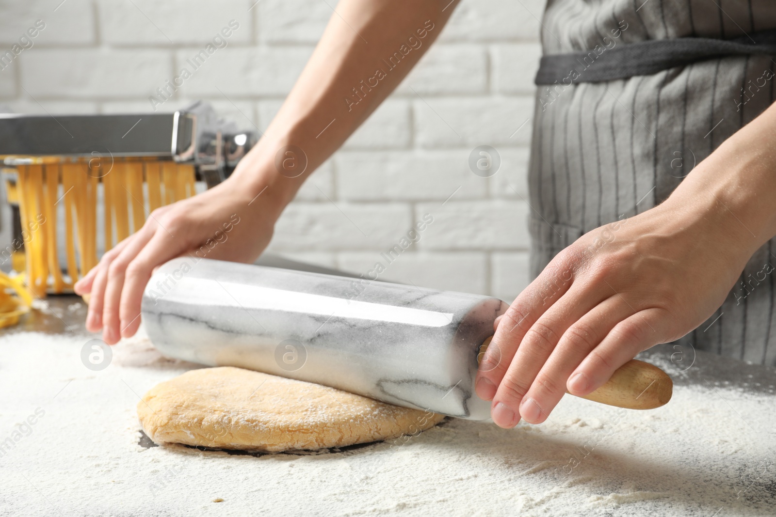 Photo of Young woman rolling dough for pasta on table