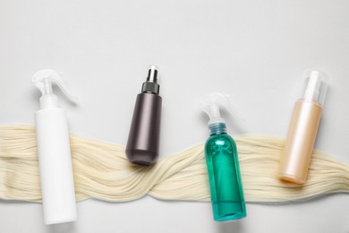 Photo of Spray bottles with thermal protection and lock of blonde hair on light background, flat lay