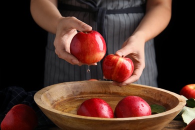 Photo of Woman washing ripe red apples in bowl of water at table, closeup