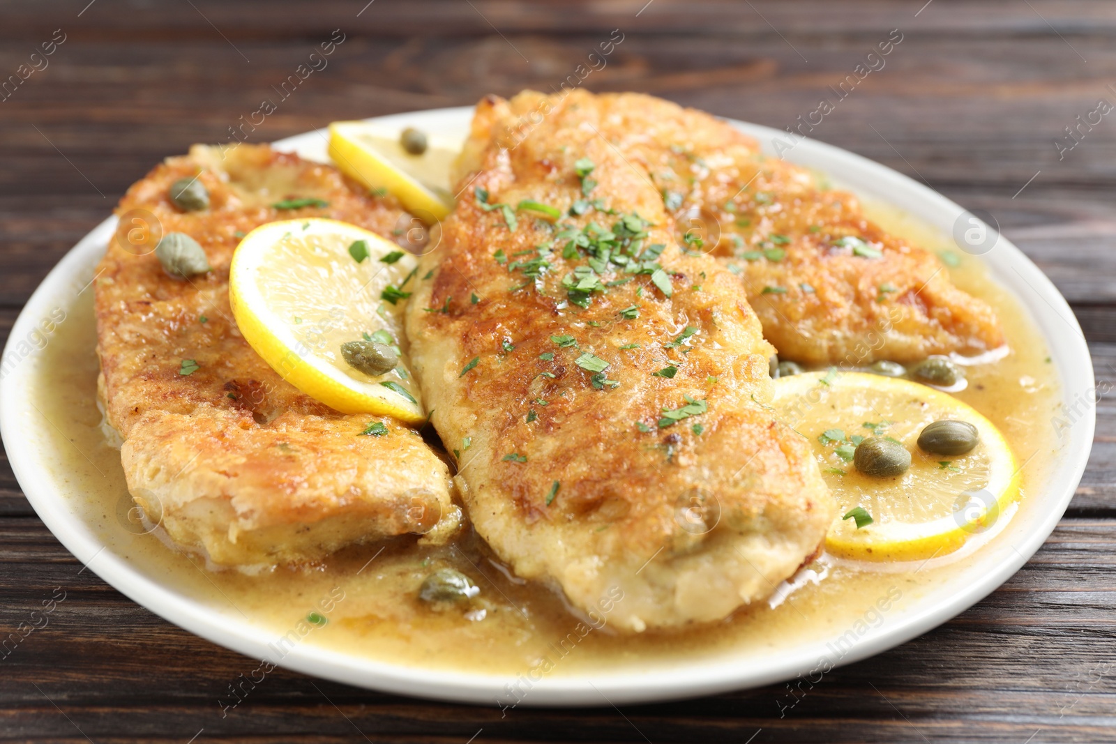 Photo of Delicious chicken piccata on wooden table, closeup