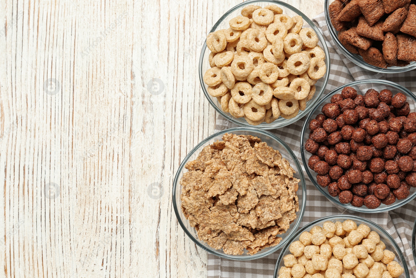 Photo of Different breakfast cereals in glass bowls on white wooden table, flat lay. Space for text