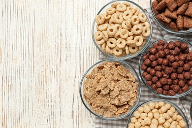 Photo of Different breakfast cereals in glass bowls on white wooden table, flat lay. Space for text