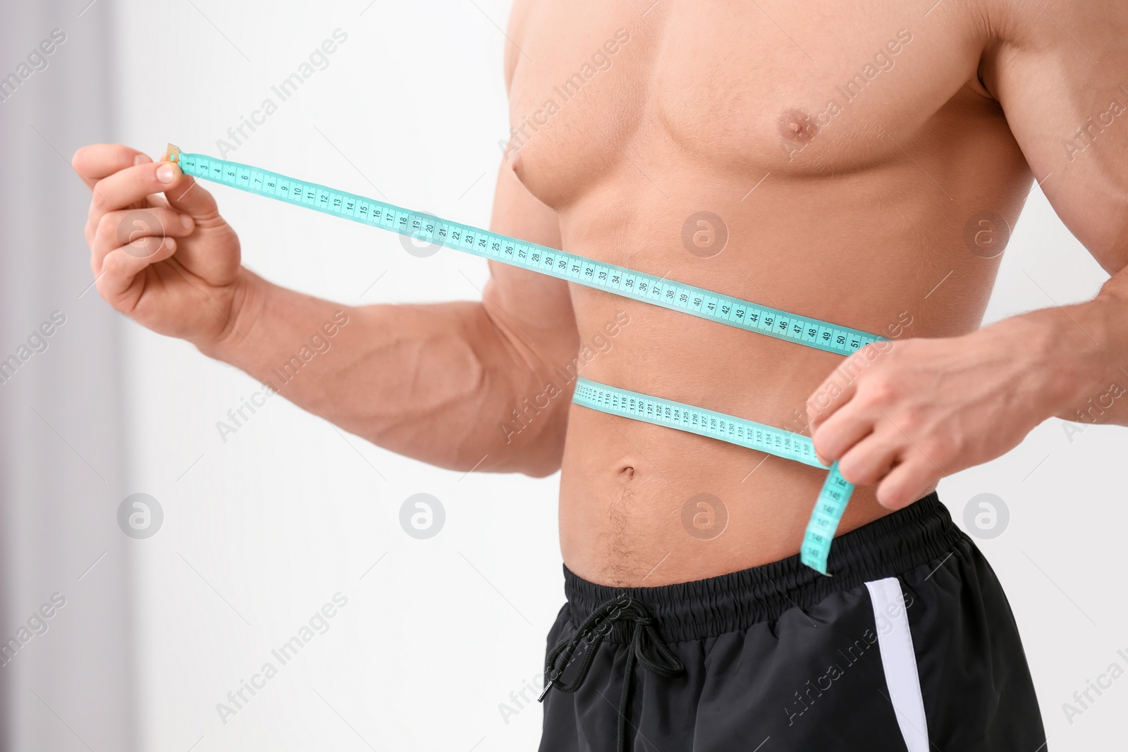 Photo of Athletic man measuring waist with tape at home, closeup. Weight loss concept