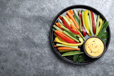 Photo of Fresh raw vegetable sticks and sauce on grey table, top view. Space for text