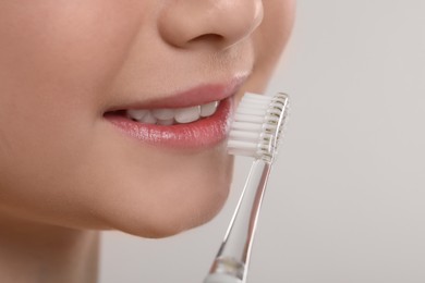 Girl brushing her teeth with electric toothbrush on light grey background, closeup. Space for text