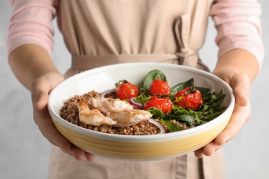 Photo of Woman holding bowl of buckwheat porridge with meat and vegetables, closeup