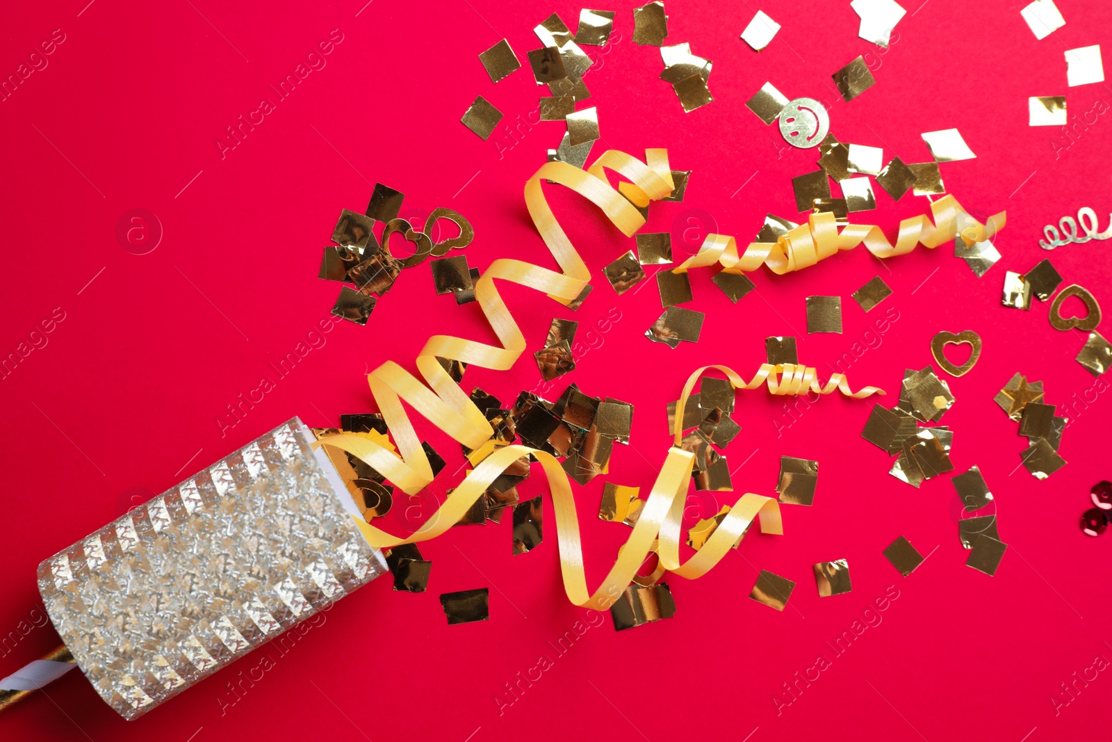 Photo of Golden confetti and streamers with party cracker on red background, top view