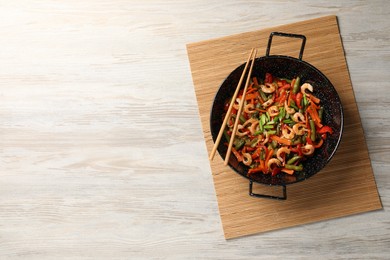 Photo of Shrimp stir fry with vegetables in wok and chopsticks on wooden table, top view. Space for text