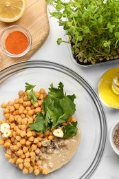 Bowl with different ingredients on white table, flat lay. Cooking delicious hummus