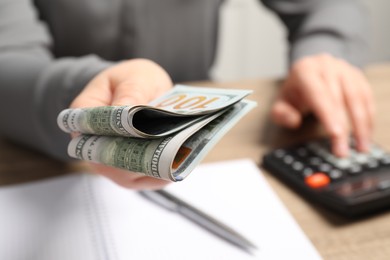 Photo of Money exchange. Woman holding dollar banknotes at wooden table, closeup