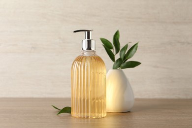 Photo of Stylish dispenser with liquid soap and green leaves in vase on wooden table
