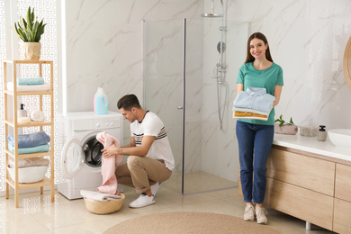 Photo of Happy couple with clean clothes in bathroom. Laundry day