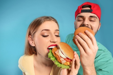 Happy couple eating burgers on color background