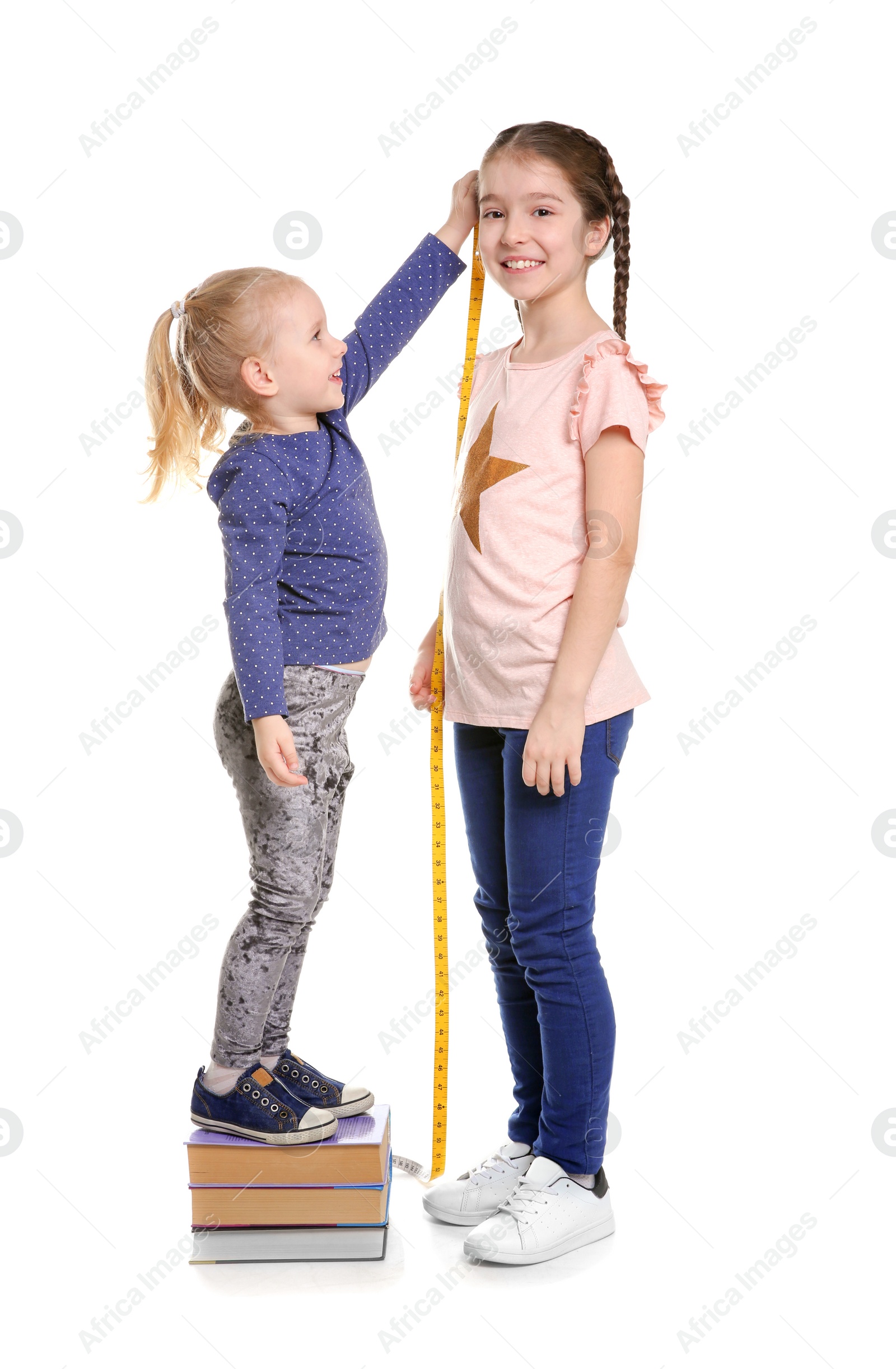 Photo of Little girls measuring their height on white background