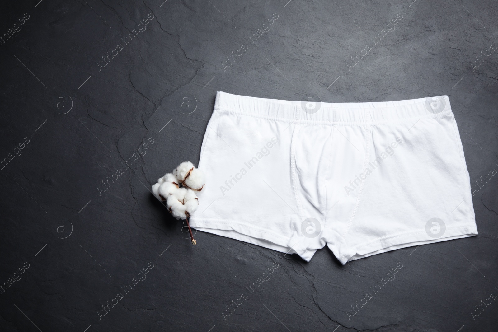 Photo of Comfortable men's underwear and cotton flowers on black stone background, flat lay