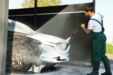 Worker washing auto with high pressure water jet at outdoor car wash