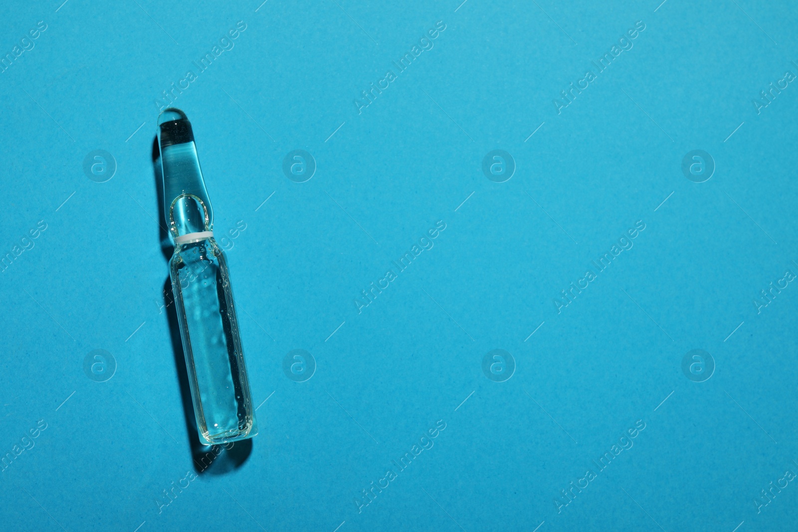 Photo of Pharmaceutical ampoule with medication on light blue background, top view. Space for text