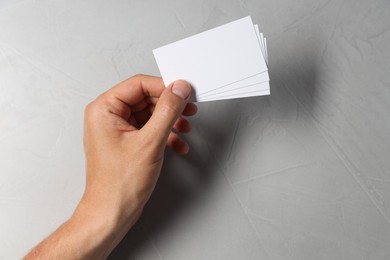 Man holding white blank cards at light grey table, top view. Mockup for design