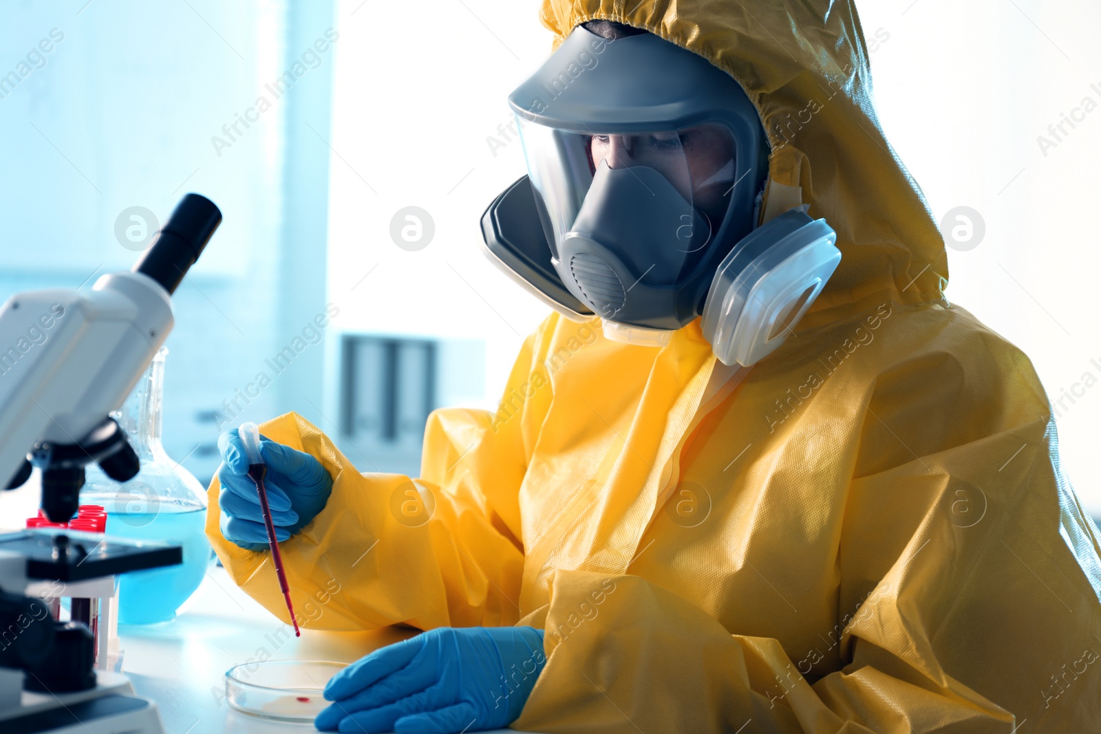 Photo of Scientist in chemical protective suit dripping blood sample into Petri dish at laboratory. Virus research