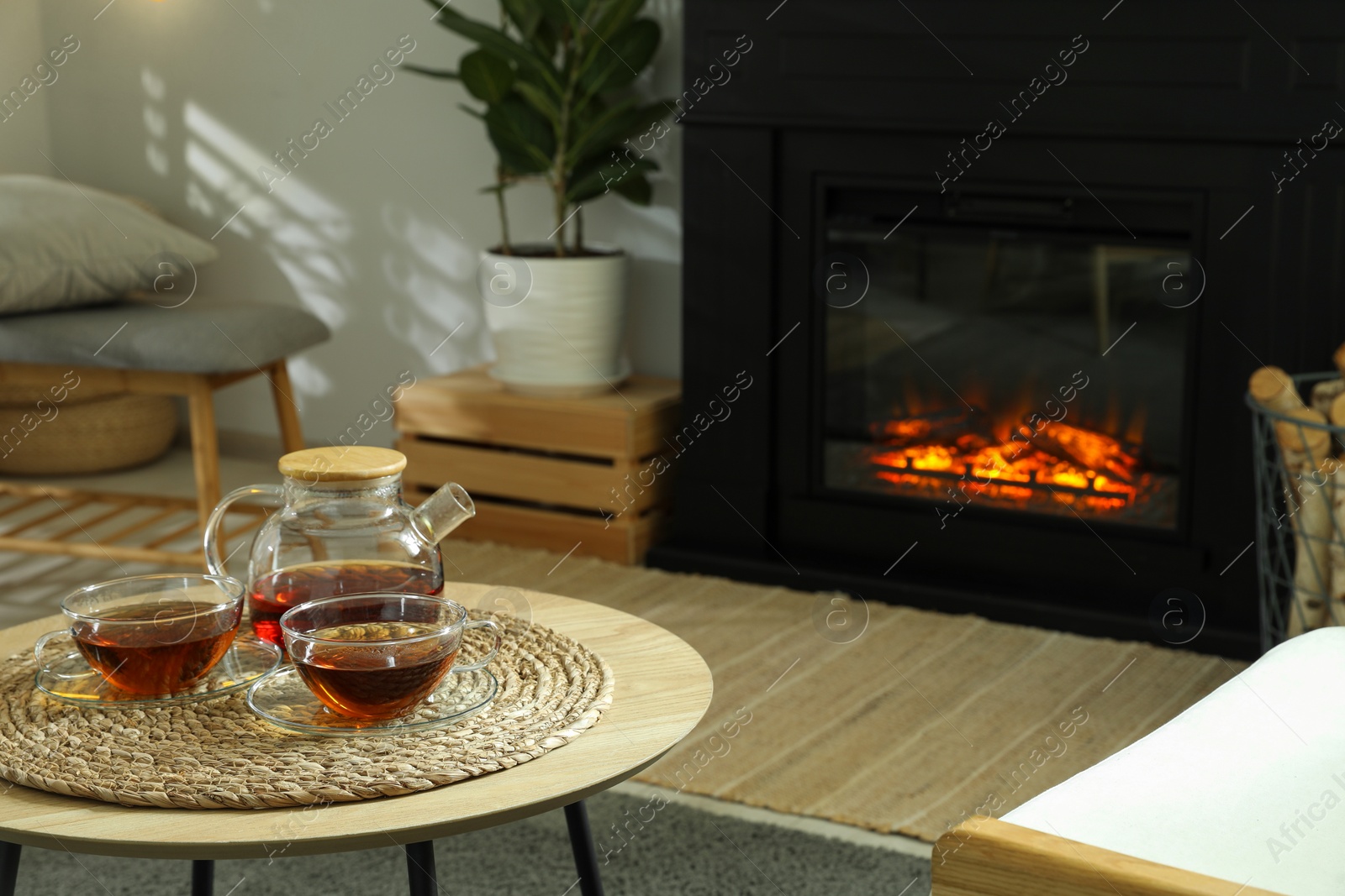 Photo of Teapot and cups of drink on coffee table near stylish fireplace in cosy living room. Interior design