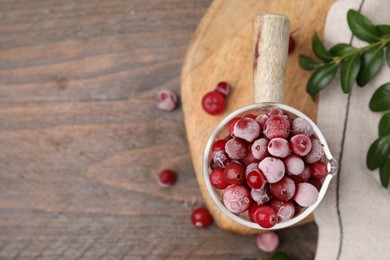 Photo of Frozen red cranberries in glass pot and green leaves on wooden table, top view. Space for text