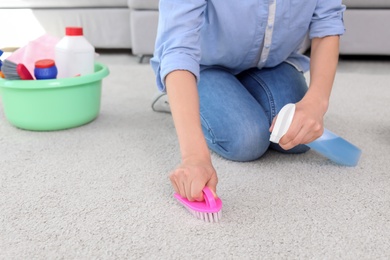 Photo of Woman cleaning carpet with brush at home