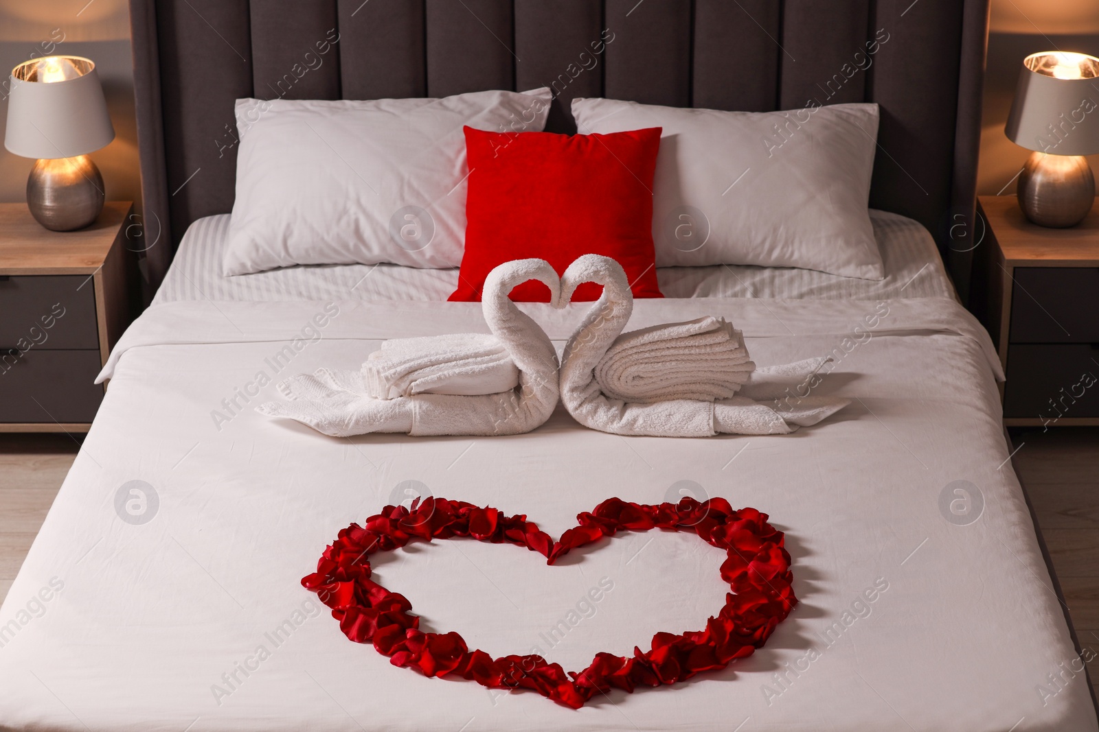 Photo of Honeymoon. Swans made with towels and heart of beautiful rose petals on bed in room