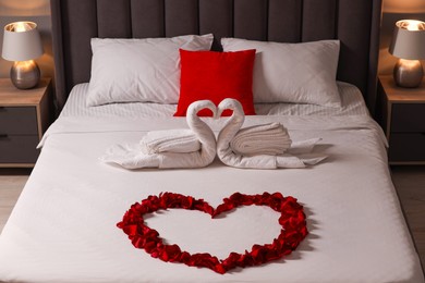 Honeymoon. Swans made with towels and heart of beautiful rose petals on bed in room