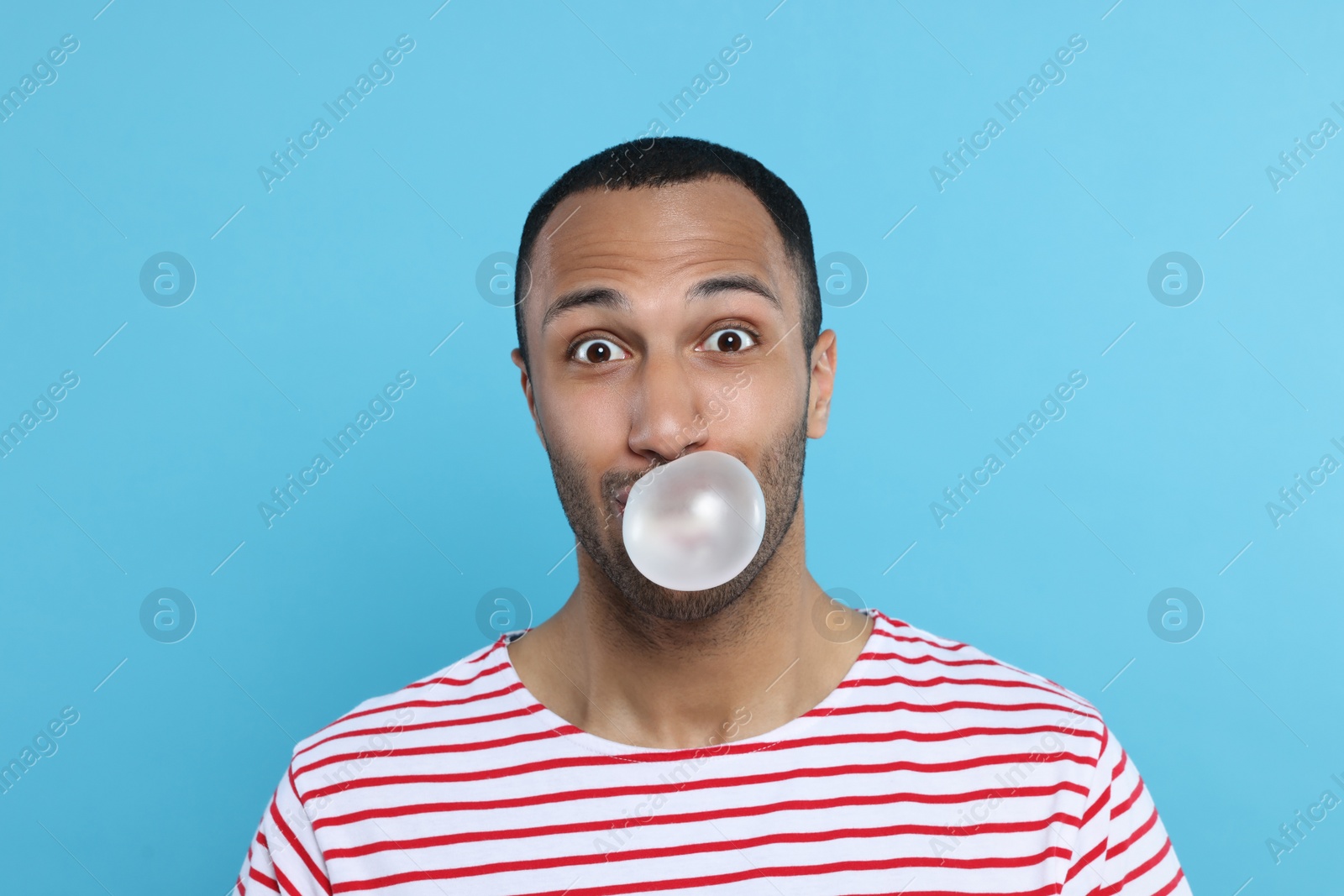 Photo of Portrait of young man blowing bubble gum on light blue background