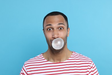 Portrait of young man blowing bubble gum on light blue background