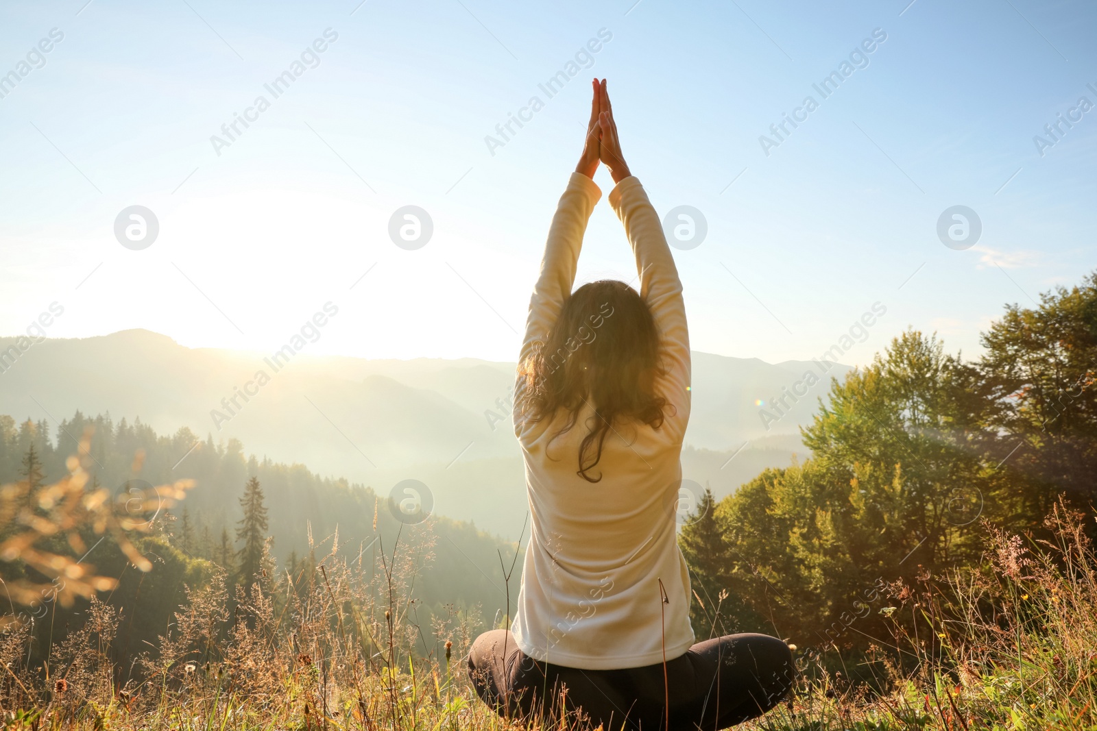 Photo of Woman practicing yoga in mountains at sunrise, back view
