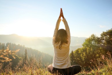 Woman practicing yoga in mountains at sunrise, back view
