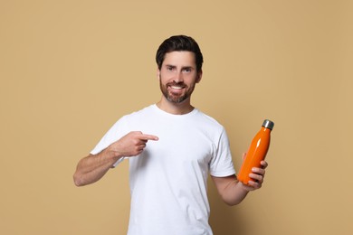 Photo of Man pointing at orange thermo bottle on beige background