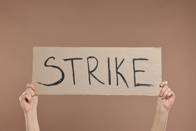 Photo of Woman holding cardboard banner with word Strike on brown background, closeup