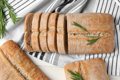 Photo of Delicious ciabattas with rosemary on beige wooden table, flat lay