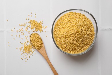 Photo of Millet groats in bowl and spoon on white tiled table, flat lay