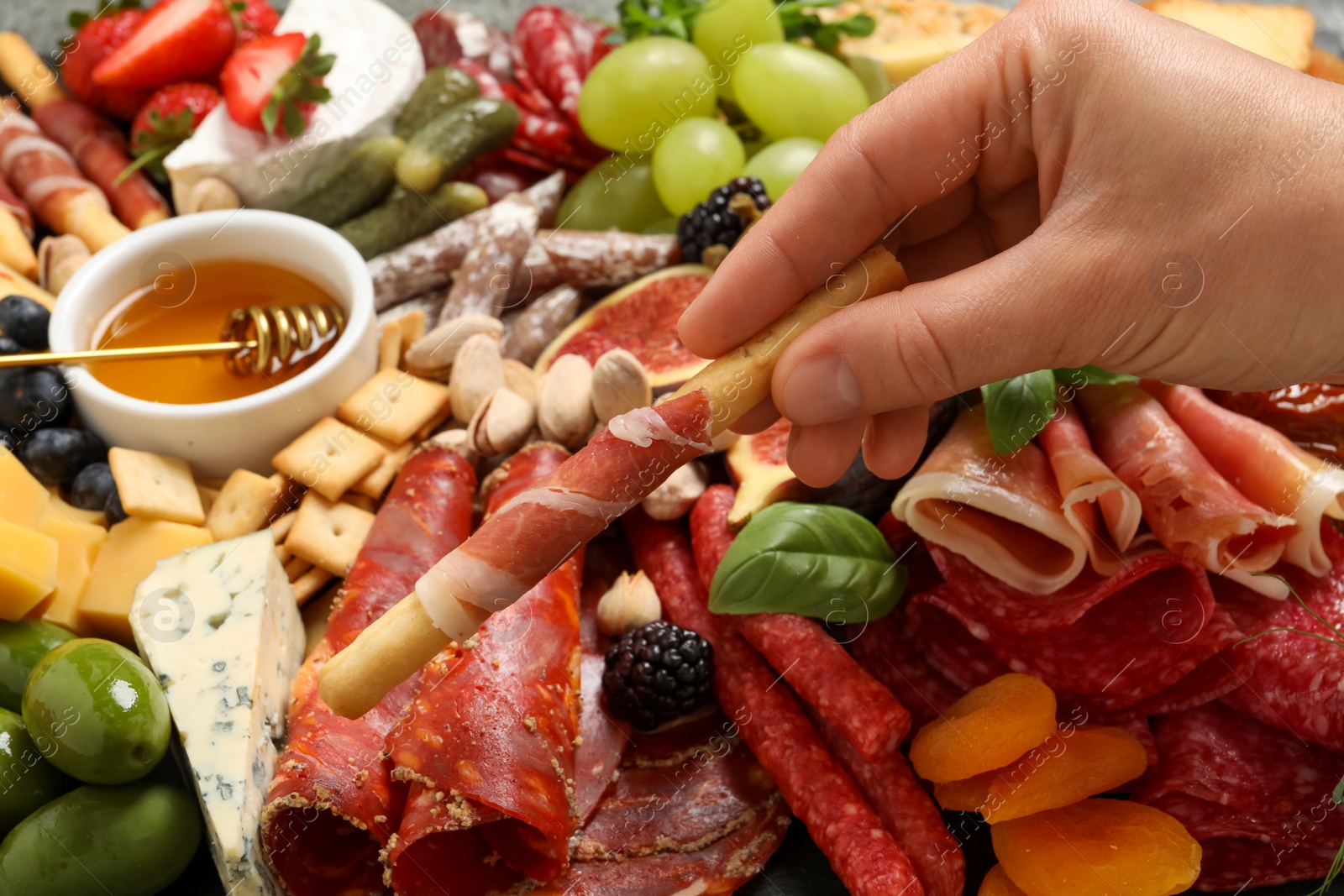 Photo of Woman taking grissini wrapped in prosciutto from set of appetizers, closeup