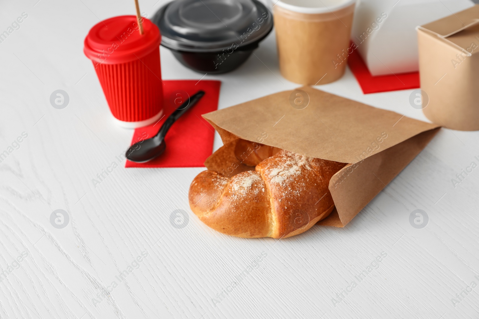 Photo of Paper bag with pastry and takeaway food on wooden table. Space for text