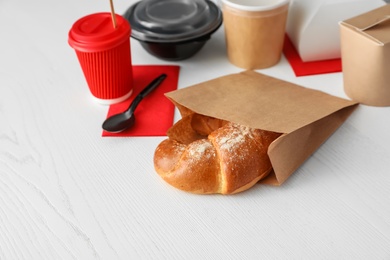 Paper bag with pastry and takeaway food on wooden table. Space for text