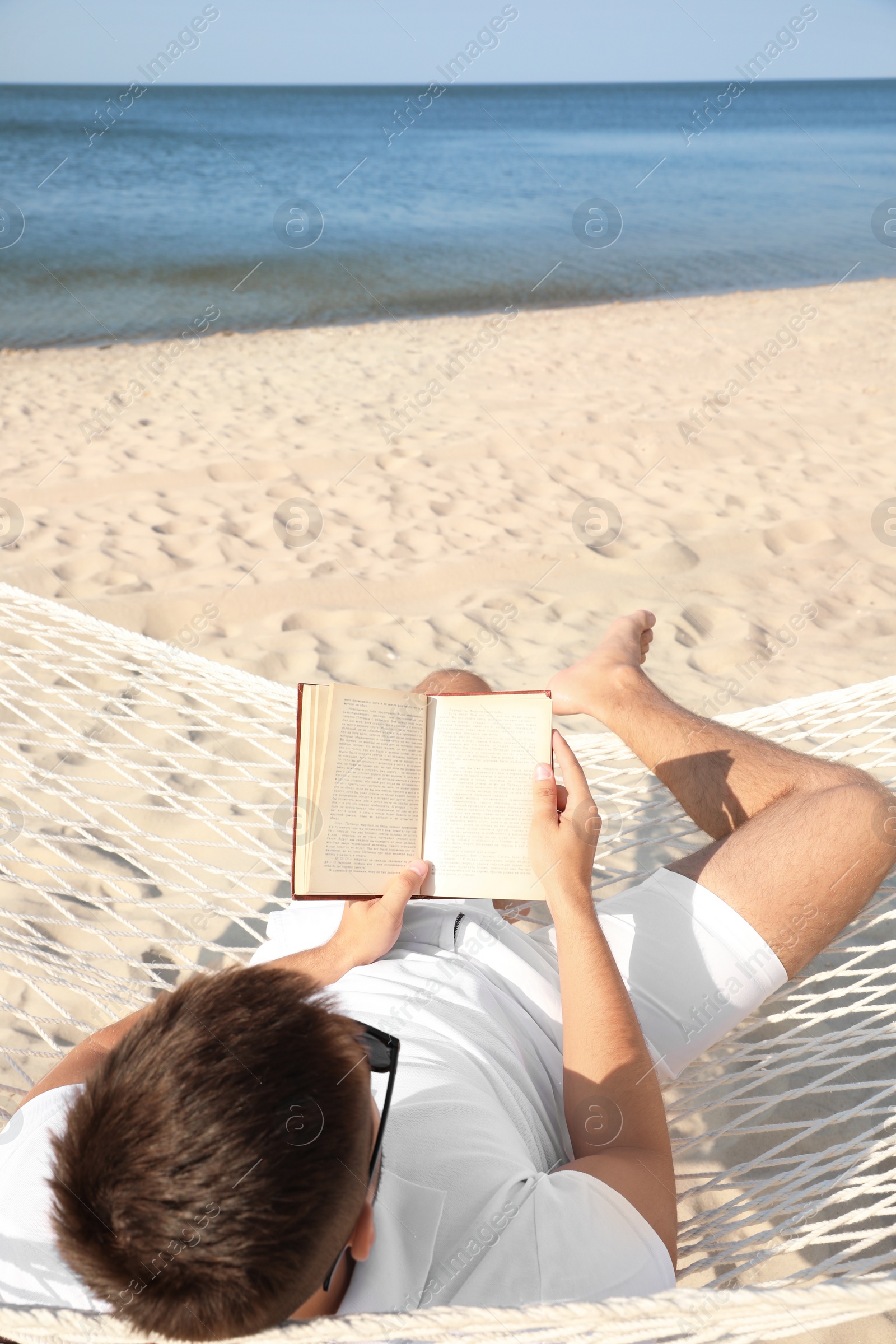 Photo of Young man reading book in hammock on beach